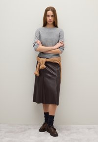 Grijze gebreide trui, bruin leren midi-rok, tan gebreide wikkel om de taille, donkerblauwe sokken en bruine veterschoenen. Gladde texturen, gestructureerd ontwerp.