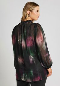 Blusa nera trasparente con motivo floreale in rosa e verde. Caratterizzata da maniche lunghe e gonfie e un collo arricciato per una vestibilità ampia.