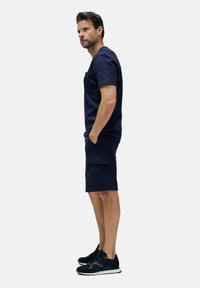 Camiseta de algodón azul marino de manga corta con un bolsillo, combinada con pantalones cortos cargo azul marino que tienen bolsillos laterales y zapatillas deportivas negras.