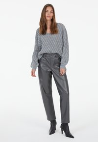 Grauer Strickpullover mit Rippenmuster, kombiniert mit hoch taillierten schwarzen Kunstlederhosen und spitzen schwarzen Absatzschuhen.