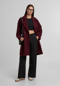 Abrigo de lana burdeos de mezcla, de doble botonadura y con amplias solapas, combinado con un top negro corto y pantalones de tiro alto; lleva zapatillas blancas.