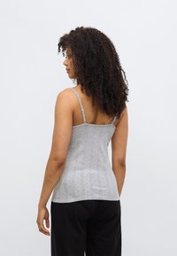 Débardeur gris en maille avec de fines bretelles, présentant un motif texturé et une coupe ajustée, associé à un pantalon noir.