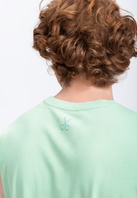 Chemisier sans manches vert menthe en coton doux. Présente un motif de ciseaux brodé discret au dos, près de l'encolure.