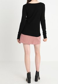 Maglione nero a maniche lunghe con una vestibilità rilassata, abbinato a una gonna in velluto a coste color rosa chiaro. L'outfit è completato da stivali neri con tacco alla caviglia.