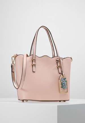 Jasnoróżowa skórzana torebka z podwójnymi uchwytami, odpinanym paskiem na ramię, falistym górnym brzegiem oraz zdobionym kwiatowym zawieszką z biżuterią.