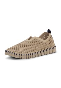 Chaussure beige à enfiler avec motif perforé festonné, détail élastique sur le côté, semelle segmentée flexible et languette de talon noire.