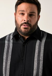 Černá flanelová košile se šedými vertikálními pruhy. Má límečkový výstřih, zapínání na knoflíky a texturovanou tkaninu.