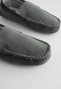 Chaussons gris texturés avec un bord tressé et un dessus en tissu doux, conçus dans un style facile à enfiler et avec un bout arrondi.