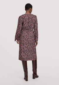 Langärmliges Kleid mit einem pinken und burgunderfarbenen Tiermuster, tailliertem Bund und Schlüsselloch-Detail im Rücken, kombiniert mit knielangen braunen Stiefeln.