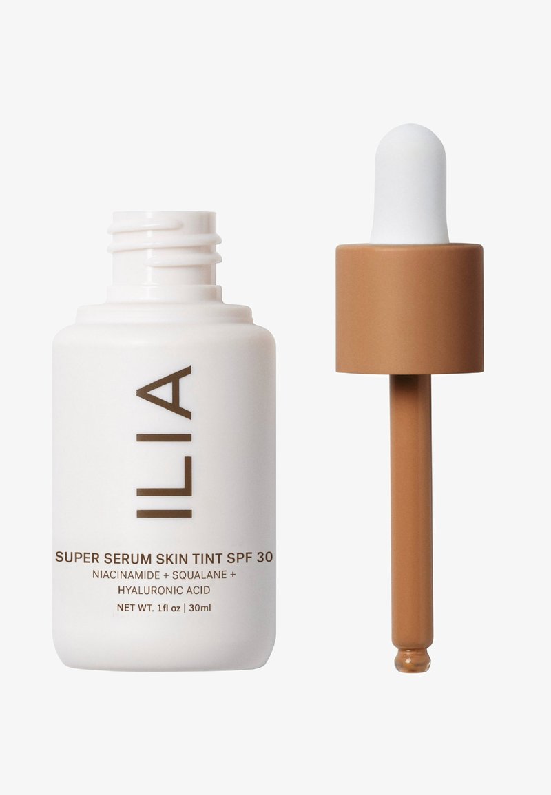 Vit glasflaska med ett brunt dropparkap, märkt "Super Serum Skin Tint SPF 30", vilket indikerar en lätt, tonad serumformulering.