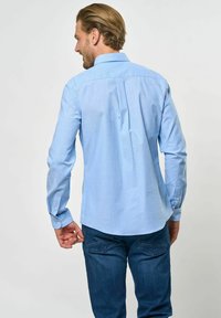 Világoskék gombos ing hosszú ujjal, egyenes aljjal és hátoldali redőzéssel, sötétkék farmernadrággal párosítva.