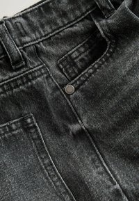 Blugi din denim gri închis cu cusături vizibile, închidere cu nasture metalic și buzunare. Țesătura are o textură subtilă și un luciu ușor.