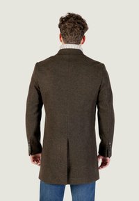 Cappotto di lana marrone con vestibilità sartoriale, apertura posteriore e polsini a tre bottoni, abbinato a un colletto a coste grigio chiaro, indossato sopra jeans blu.