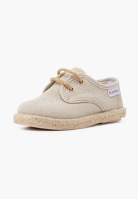Chaussure pour enfant en toile beige avec un bout arrondi, détail tissé sur la semelle, et lacets marron passés à travers des œillets en métal.