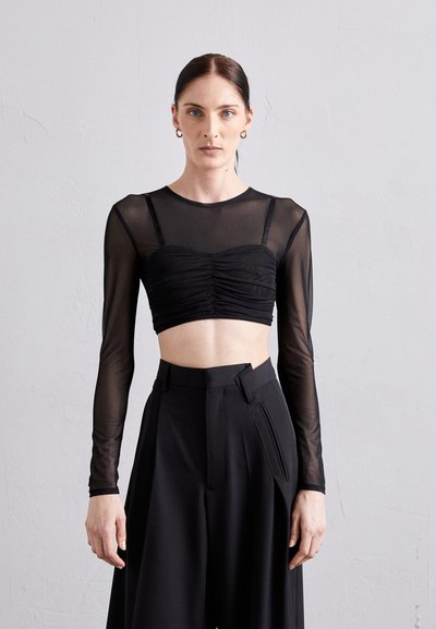 Haut noir court avec des manches longues transparentes et des détails froncés au niveau de la poitrine, associé à un pantalon noir taille haute avec des plis.