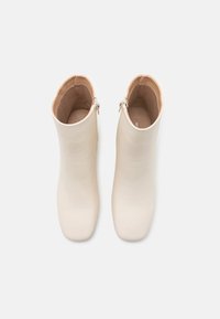 Bottes blanches chevilles en cuir lisse, bout arrondi, avec une fermeture éclair latérale. Intérieur doublé beige pour un confort supplémentaire.
