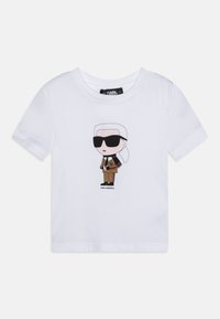 Balts īsām piedurknēm t-krekls ar karikatūras grafiku, kurā attēlots tēls brilles un brūnā mētē, ar melniem akcentiem un zīmola etiķeti.