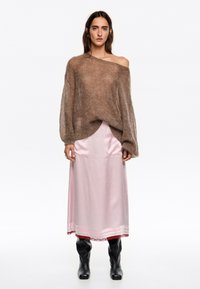 Brązowy, dzianinowy sweter z dekoltem off-the-shoulder; w zestawie z długą, jasnoróżową satynową spódnicą z ozdobnym wykończeniem. Czarne botki.