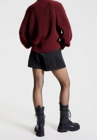 Burgundy knitted sweater, black mini skirt, fishnet tights, and black combat boots with thick soles and lace-up details.