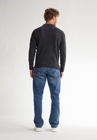 Sweater en tricot gris foncé avec un col rond, associé à un jean bleu clair. Des baskets blanches complètent la tenue. Ourlet côtelé visible sur le sweater.