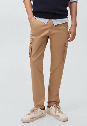 Pantalones cargo beige con bolsillos laterales, corte recto, hechos de tela suave. Combinados con un suéter azul marino sobre una camisa con cuello. Zapatillas neutras.