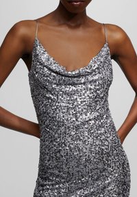 Robe en sequins argentés avec un col bénitier, des bretelles fines et une coupe ajustée, mettant en valeur une texture réfléchissante et des détails complexes sur toute la surface.