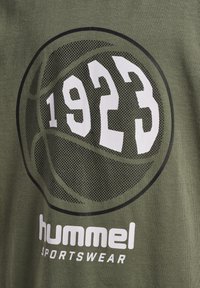 Zielona bawełniana koszulka z dużą czarną grafiką koszykówki o siateczkowej teksturze oraz białym napisem "1923" i logiem "hummel sportswear" poniżej.