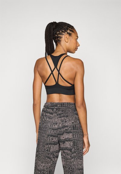 Sujetador deportivo negro con diseño de espalda cruzada, combinado con pantalones oscuros de estampado con textura parecida a la del cocodrilo.