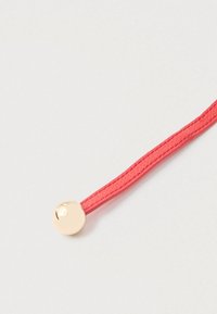 Czerwony pasek ze sk�óry z małym, okrągłym, polerowanym złotym metalowym guzikiem przymocowanym na jednym końcu na jasnym tle.