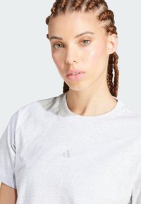 Camiseta de algodón gris con cuello redondo y mangas cortas. Presenta un logo sutil en gris claro en el pecho. Textura suave.