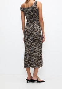 Robe longue à motif léopard, tissu extensible, design asymétrique à une épaule, silhouette ajustée, longueur mi-mollet, associée à des sandales noires à talons.