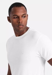 Biała koszulka z okrągłym dekoltem i krótkimi rękawami, wykonana z gładkiego materiału, z dyskretnym logo na piersi i luźnym krojem.