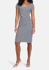Striped knee-length dress in navy and white, featuring a wrap design, short sleeves, and a fitted silhouette. Paired with white heeled sandals.