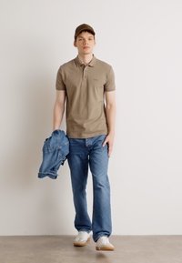 Bež polo majica, plave traperice i bijele tenisice. Jakna se drži u jednoj ruci. Smeđa kapa upotpunjuje outfit. Jednostavan, ležeran dizajn.