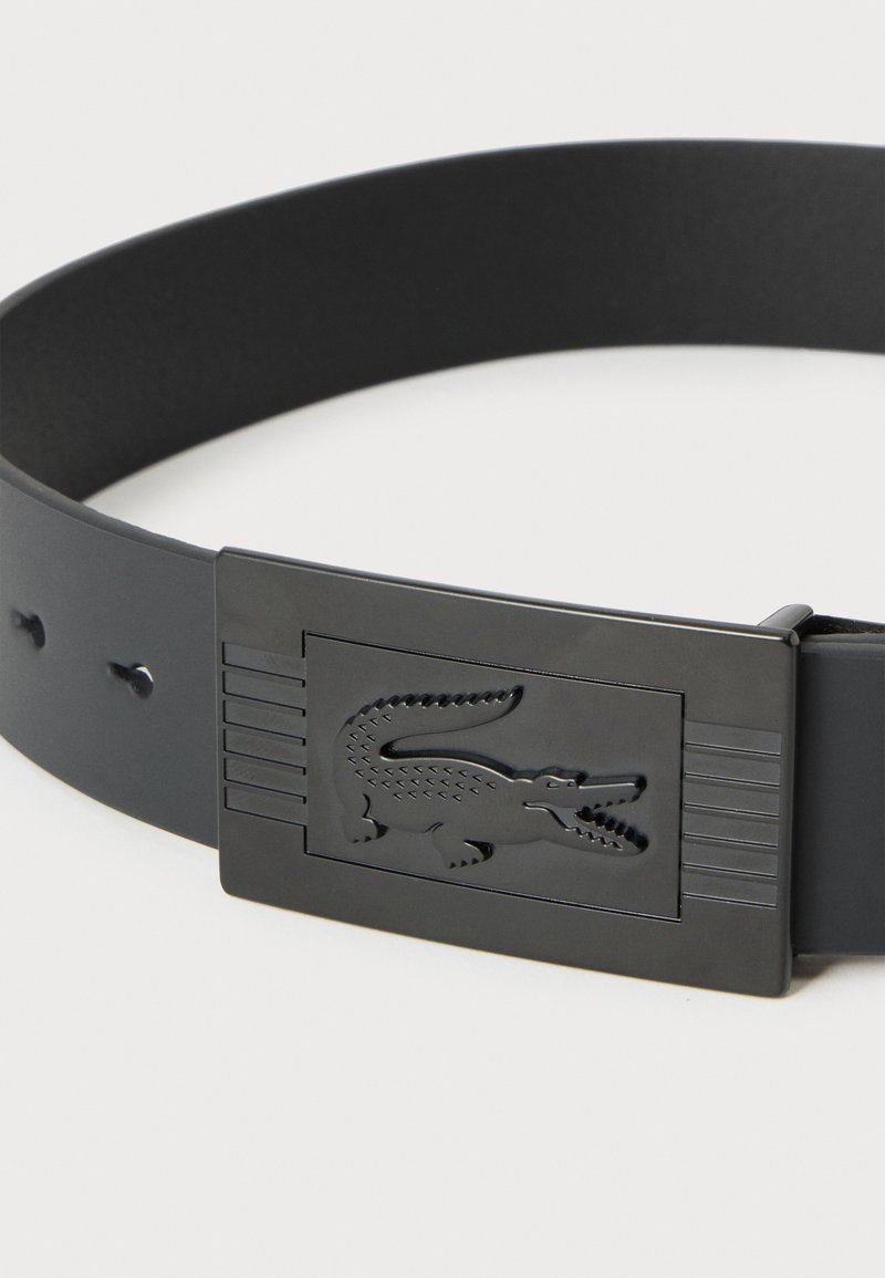 Black belt with rectangular black buckle featuring embossed crocodile logo and horizontal engraved lines on each side.