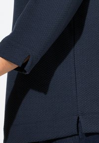 Top strutturato blu navy con texture e motivo a rombi, maniche a tre quarti con aperture e orlo dritto.
