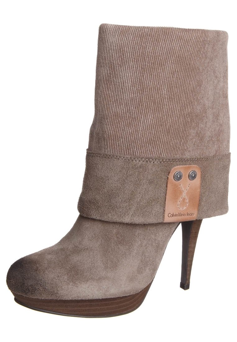 Zamszowe botki za kostkę w jasnobrązowym kolorze z prążkowanym mankietem, wysokim obcasem oraz skórzanym oznaczeniem z tłoczonym logo i metalowymi akcentami.