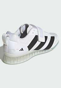 Weißer Sneaker mit schwarzen Streifen, strukturiertem Obermaterial, verstellbarem Klettverschlussriemen und transparentem, gemustertem Profil. Sichtbare Maße des gestuften Absatzes.