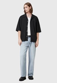 Camicia nera a maniche corte con bottoni sopra una canotta bianca, abbinata a jeans boyfriend blu chiaro e scarpe nere. Collana d'argento come accessorio.