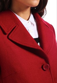 Abrigo de mezcla de lana rojo con cuello de muesca y cierre con un solo botón rojo. Presenta una textura suave y un diseño estructurado.
