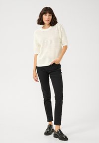 Pull en maille blanc à manches courtes avec un motif texturé, associé à un pantalon noir slim-fit et des mocassins noirs. Design simple et épuré.