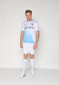 Completo da calcio maschile con una maglietta gradient blu chiaro e bianca con un logo, abbinata a pantaloni corti bianchi e calzettoni bianchi al ginocchio.