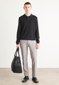 Črn polo s dolgimi rokavi, sivi krojeni hlače, črni usnjeni čevlji, drži črno-sivo torbo za vikend, minimalno blagovno znamko na polo majici.