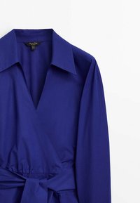 Djupblå omlottklänning i mjukt tyg, med spetskrage, långa ärmar och midjeband för justering.