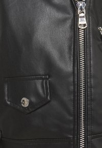 Czarna skórzana kurtka, zbliżenie na srebrny zamek błyskawiczny, małą kieszeń z klapką i detale z metalowym zatrzaskiem.