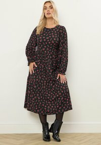 Svart blommig midiklänning med långa ärmar, med en lager-på-lager kjol och små röda blommönster, kombinerad med blanka svarta ankelstövlar.