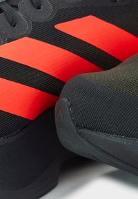 Black athletic shoe with three prominent red stripes, textile upper, textured black accents, and a rounded, cushioned sole.