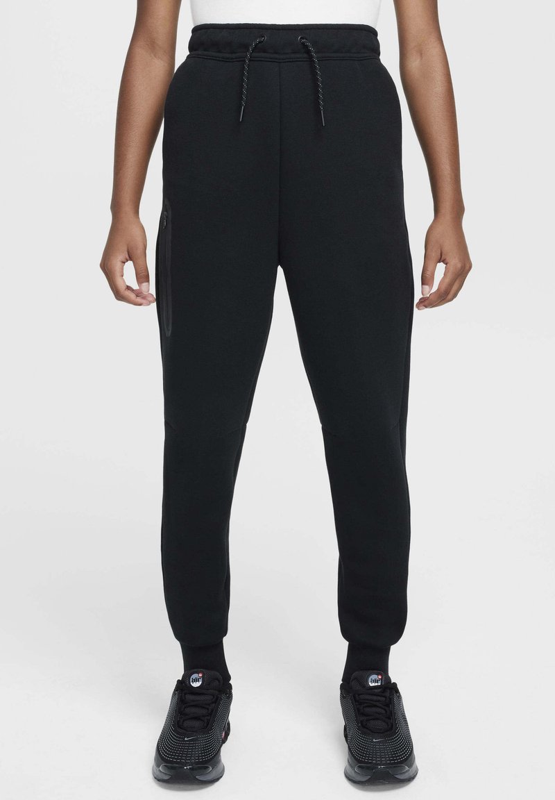 Pantalon de survêtement noir en tissu doux, avec taille à cordon, poches latérales zippées, jambes effilées et poignets côtelés.