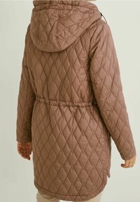 Brun quiltet lang jakke med hætte, elastisk talje og diamantsting, vist bagfra på en person med lyse bukser.