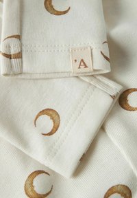 Heled kreemkangas, millel on väikesed, roostes värvi poolkuu mustrid. Sisaldab kootud silti, millel on täht "A". Sile tekstuur ja korralik õmblus.